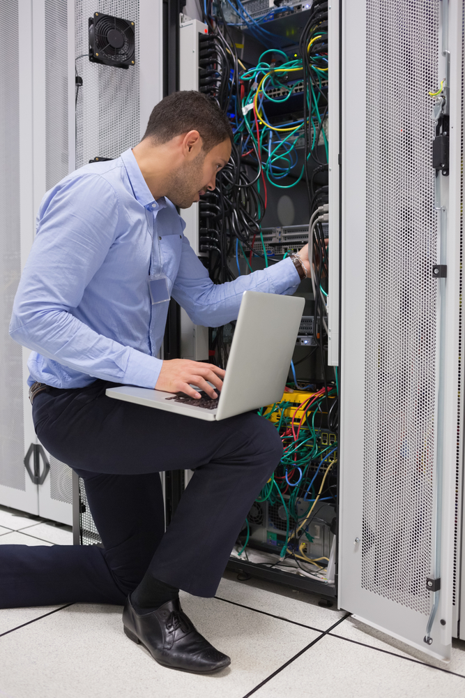 Man fixing wires while doing maintenance with laptop in data center Man fixing wires while doing maintenance with laptop in data center