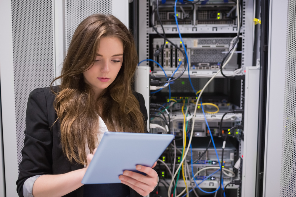 Woman using tablet pc in front of servers in data center Woman using tablet pc in front of servers in data center